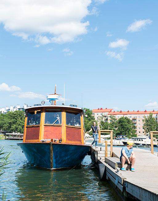 Mustasaaren lautta Taivallahden laiturissa. Taustalla kerrostaloja. Poika istuu laiturilla.